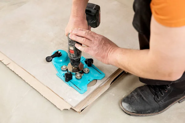 A tiler uses a caliper with a suction cup to drill holes in the ceramic tile