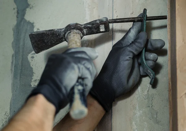 Woker hammers a nail with a foot into a wall — Stock Photo, Image