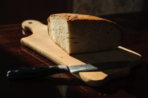 Homemade bread on a board and knife on dark background — Stock Photo, Image