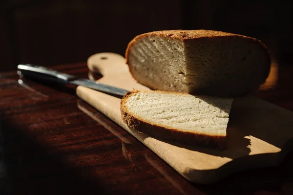 Homemade bread on a board and knife on dark background — Stock Photo, Image