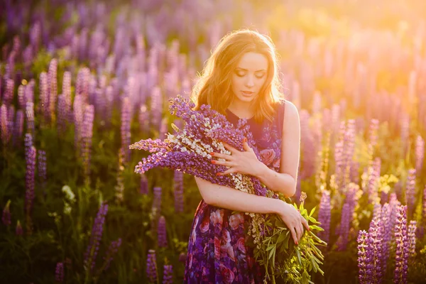 Chica en el campo de flores silvestres púrpura, puesta de sol en el día soleado — Foto de Stock