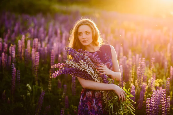 Chica en el campo de flores silvestres púrpura, puesta de sol en el día soleado — Foto de Stock