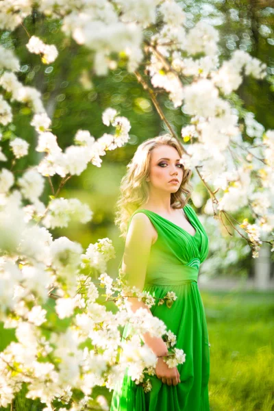 Beautiful young blond woman standing beside a blossoming Apple tree — Stock Photo, Image