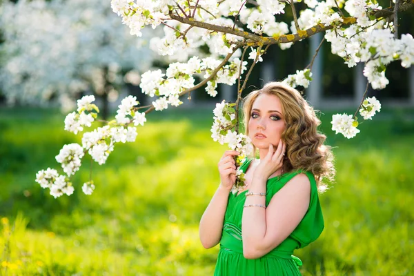 Beautiful young blond woman standing beside a blossoming Apple tree — Stock Photo, Image