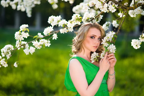 Schöne junge blonde Frau steht neben einem blühenden Apfelbaum — Stockfoto