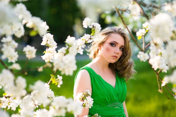 Hermosa joven rubia de pie junto a un manzano floreciente — Foto de Stock