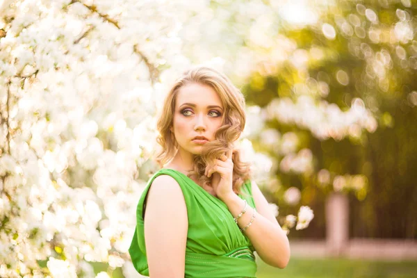 Hermosa joven rubia de pie junto a un manzano floreciente — Foto de Stock