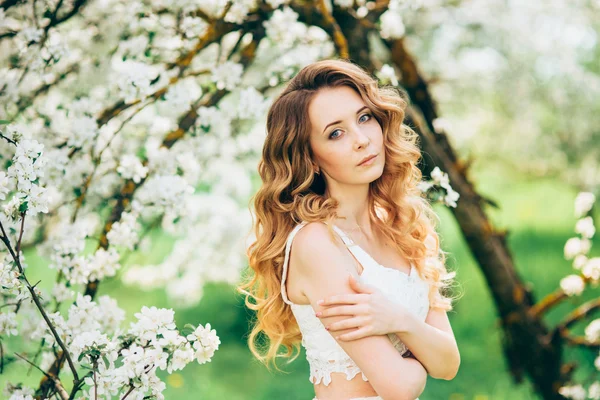 Primavera bella ragazza, bionda, in piedi in un frutteto di mele in fiore  . — Foto Stock