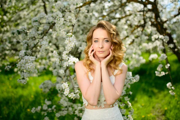 Lente mooi meisje, blond, permanent in een bloeiende boomgaard van Apple . — Stockfoto