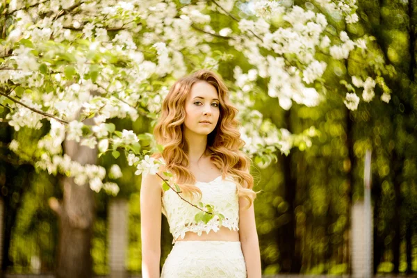 Lente mooi meisje, blond, permanent in een bloeiende boomgaard van Apple . — Stockfoto