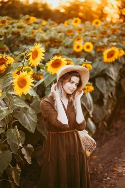 Yazın gün batımında elinde bir torba yiyecekle ayçiçeği tarlasında güzel bir kız.