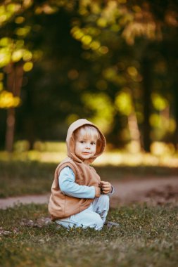 Kapüşonlu kahverengi yelekli bir çocuk akşamları sonbahar ormanında yürür.