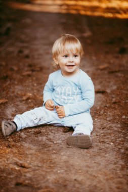 Mavi elbiseli güzel bir çocuk bir sonbahar günü parkta oturmuş birine gülümsüyor.