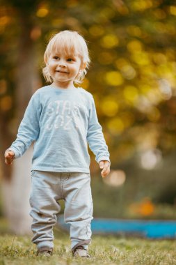 Mavi elbiseli güzel bir çocuk bir sonbahar günü parkta birine gülümsüyor ve yürüyor.