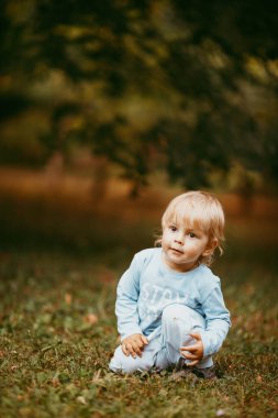 Mavi elbiseli güzel bir çocuk bir sonbahar günü parkta birine gülümsüyor ve yürüyor.