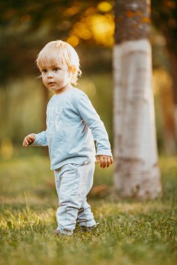 Mavi elbiseli güzel bir çocuk bir sonbahar günü parkta birine gülümsüyor ve yürüyor.
