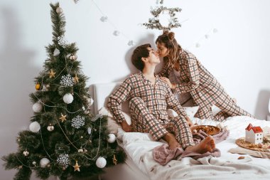 family, Christmas, holidays, love and people concept-happy couple sitting on the bed at home