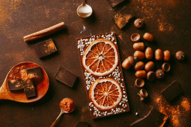 Çubukların ve portakal dilimli farklı siyah çikolataların bileşimi, kahverengi arkaplandaki baharatlar - yukarıdan görünüm