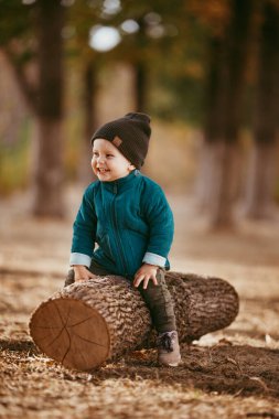 Yeşil ceketli ve örgü şapkalı bir çocuk ağaçta oturuyor. O mutlu. Seçici odaklı resim