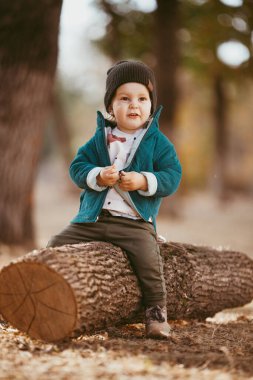 Yeşil ceketli ve örgü şapkalı bir çocuk ağaçta oturuyor. O mutlu. Seçici odaklı resim