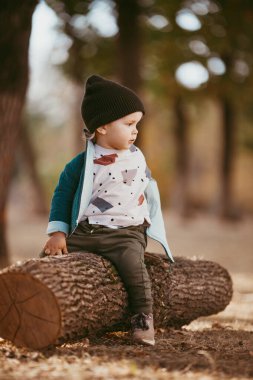 Yeşil ceketli ve örgü şapkalı bir çocuk ağaçta oturuyor. O mutlu. Seçici odaklı resim