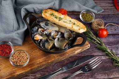 Siyah ahşap arka planda bakır mutfak kabında midyeler.