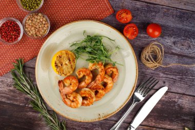 Beyaz tepside biber ve maydanoz serpilmiş tereyağlı sarımsaklı karides, ahşap bir masada, üst manzara.