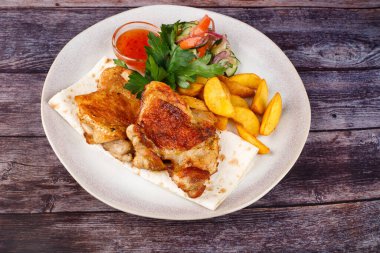 Beyaz bir tabakta patates kızartmalı tavuk, ahşap bir masanın arkasında.