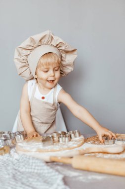 Önlük giymiş mutlu bir çocuk ve aşçı şapkası hamur hazırlar, mutfakta kurabiye pişirir.