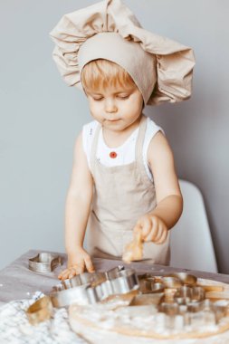 Önlük giymiş mutlu bir çocuk ve aşçı şapkası hamur hazırlar, mutfakta kurabiye pişirir.