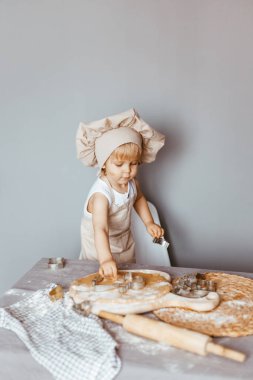 Sevimli çocuk evde mutfakta önlük ve aşçı şapkasıyla hamur hazırlıyor.