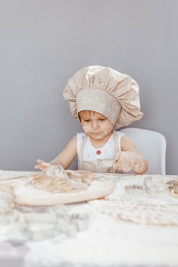 Önlük giymiş mutlu bir çocuk ve aşçı şapkası hamur hazırlar, mutfakta kurabiye pişirir.