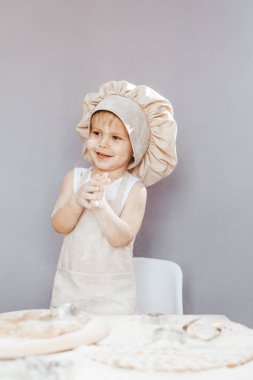 Sevimli çocuk evde mutfakta önlük ve aşçı şapkasıyla hamur hazırlıyor.