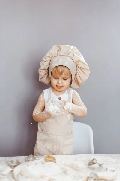エプロンの幸せな子供とシェフの帽子は生地を準備しキッチンでクッキーを焼く — ストック写真