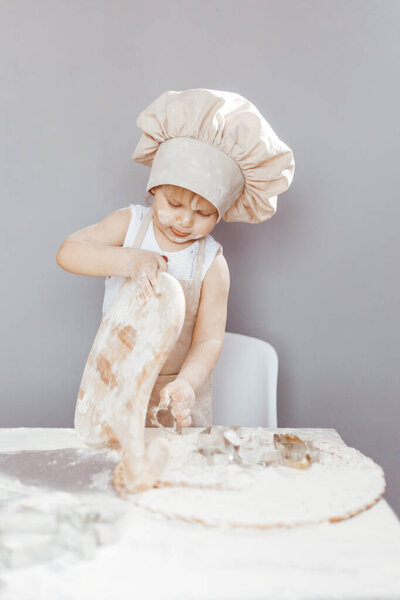 Portrait of a little cook kneading dough in an apron and a chef's hat. Cooking children's lifestyle concept
