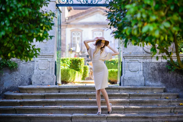 Красива молода жінка з темним волоссям в елегантній бежевій сукні позує на сходах — стокове фото