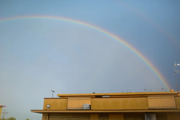 Regenboog bij zonsondergang onder huizen — Stockfoto