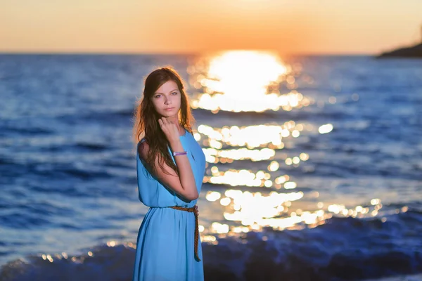 Jovem mulher de vestido na praia ao pôr do sol contra o sol — Fotografia de Stock