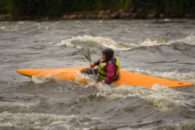 Bir adam çalkantılı bir nehirde kayıkla yüzüyor