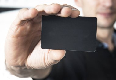 Man holding black credit card over white wall background, black card for loading content. Mockup ready