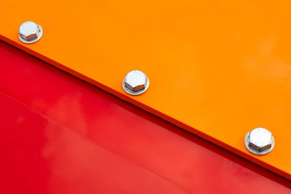 Close up of red and orange metal surface connected with steel bolts