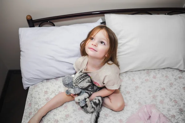 Kleines Mädchen im Bett spielt mit einem Kätzchen — Stockfoto