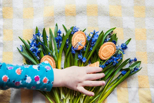 Top vies child's hand taking cookies in the shape of Easter eggs and Scilla lie on a wooden cutting board — Stock Photo, Image