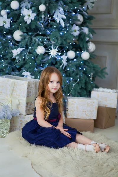 Μικρό κορίτσι σε ένα κομψό φόρεμα που κάθεται στο το χριστουγεννιάτικο δέντρο — Φωτογραφία Αρχείου