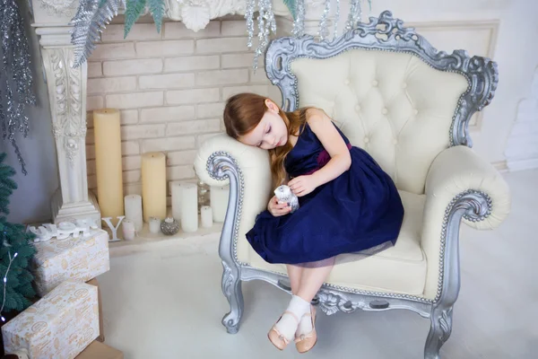 Μικρό κορίτσι σε ένα κομψό φόρεμα που κάθεται σε μια καρέκλα και χωρίς κοιτάζοντας το πλαίσιο — Φωτογραφία Αρχείου