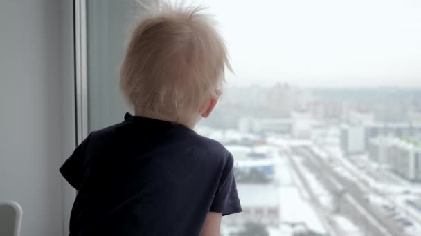 Dociekliwy śmieszne dziecko wygląda z odsetkami przez okno na ulicy — Wideo stockowe
