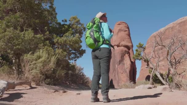 Starší aktivní žena turista s batohem vypadá kolem na červené skály v poušti — Stock video