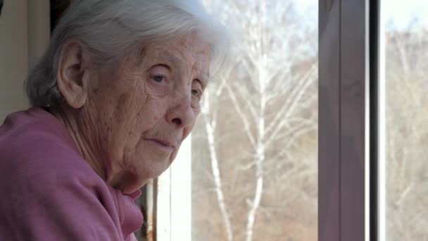 Très vieille femme caucasienne âgée avec cheveux gris regardant tristement sur la fenêtre — Video