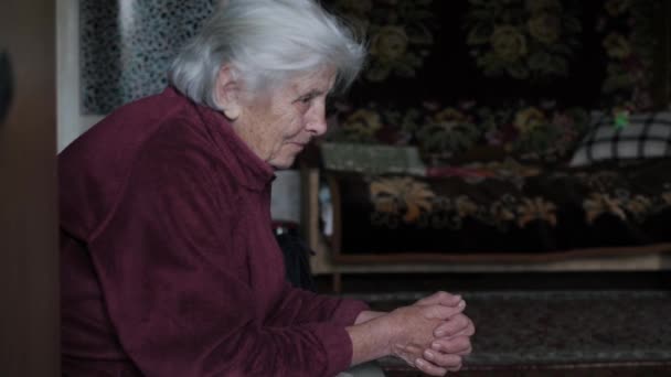 Vista lateral de una anciana mujer caucásica con temblor con el pelo gris se sienta en una silla — Vídeos de Stock