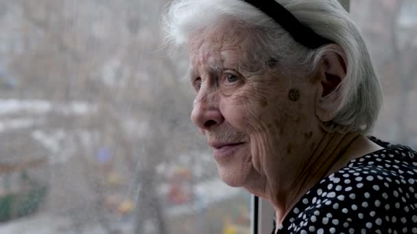 Stará starší běloška vypadá mimo okno z bytu s úrokem — Stock video